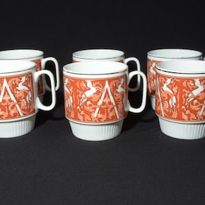 May include: Set of six white ceramic mugs with a red and white floral design. The mugs have a gold trim around the rim.