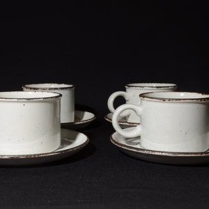 Op de afbeelding: Set van vier witte keramische koffiekopjes met bruine randen en spikkels. Elk kopje wordt geleverd met een bijpassend schoteltje.
