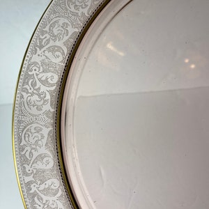 Puede incluir: Un plato de cer&aacute;mica blanco con un borde dorado y un delicado dise&ntilde;o floral en relieve alrededor del borde.