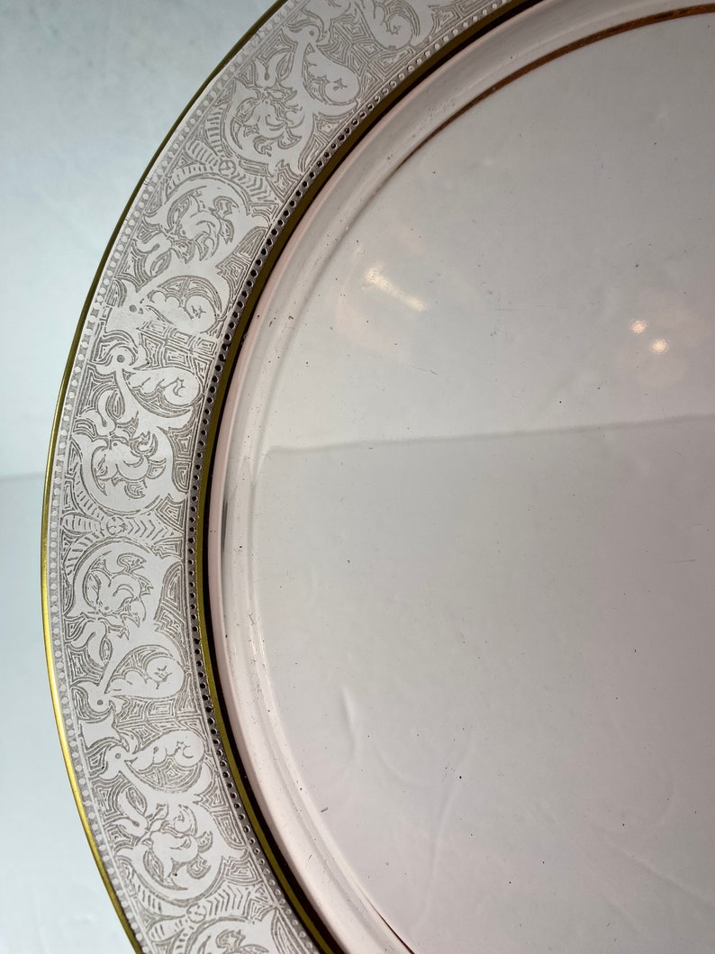 Puede incluir: Un plato de cer&aacute;mica blanco con un borde dorado y un delicado dise&ntilde;o floral en relieve alrededor del borde.
