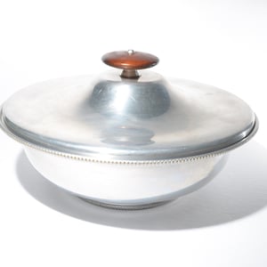 Puede incluir: Un bol de servir plateado con tapa y un pomo de madera en la parte superior. El bol tiene un borde con cuentas y un acabado brillante.