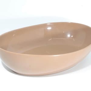 May include: A light brown, oval-shaped serving bowl. The bowl has a smooth, glossy finish and a simple, modern design. The bowl is empty and sits on a white surface.