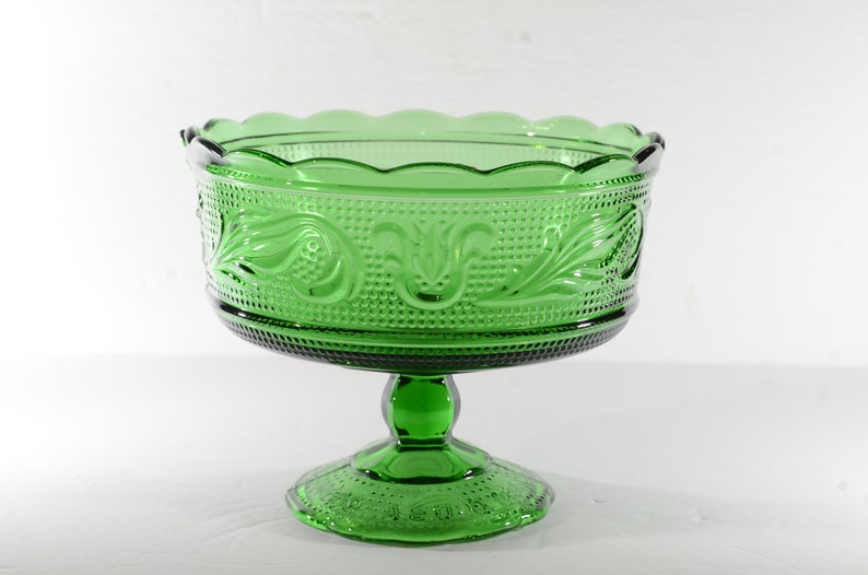 May include: A green glass pedestal bowl with a scalloped rim and a decorative floral pattern. The bowl is on a white background.