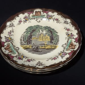 Puede incluir: Un juego de tres platos de cerámica vintage con un diseño floral marrón, dorado y blanco. El centro de cada plato presenta una escena de un edificio con árboles y un puente.