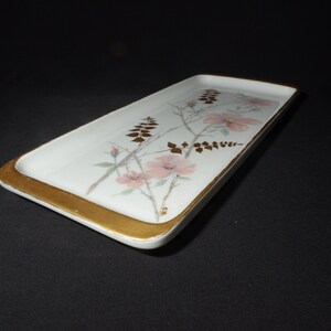 May include: Rectangular white serving tray with a gold rim and floral design. The tray features pink flowers and gold accents on a white background. A decorative piece for serving or display.