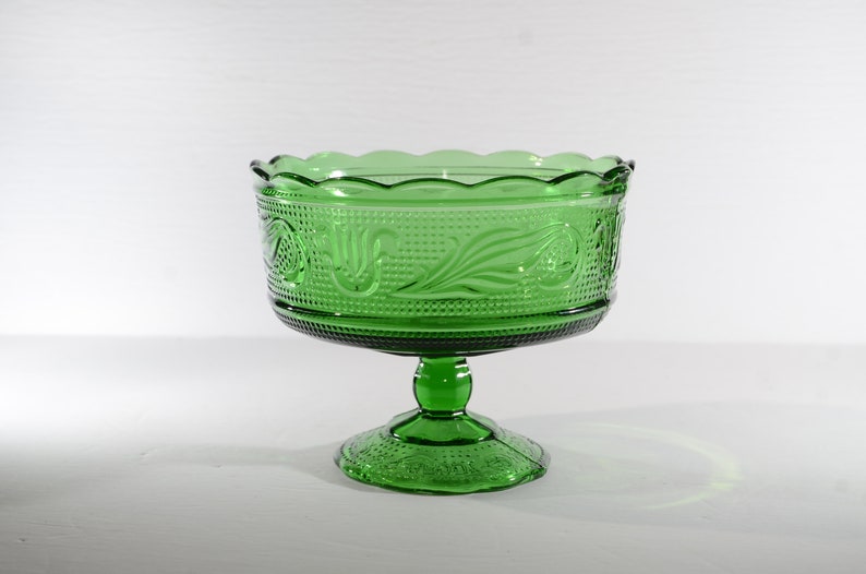 May include: A green glass pedestal bowl with a scalloped rim and an embossed floral design.