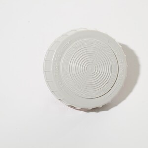 May include: A light gray plastic lid with concentric circular ridges and the words "TO TIGHTEN" and "TO REMOVE" embossed around the edge. The lid is designed to screw onto a container.