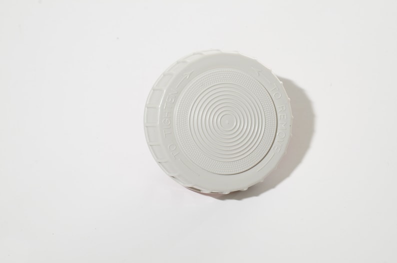 May include: A light gray plastic lid with concentric circular ridges and the words "TO TIGHTEN" and "TO REMOVE" embossed around the edge. The lid is designed to screw onto a container.