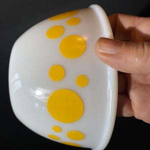 May include: White ceramic bowl with yellow polka dots. The bowl is slightly tilted and the polka dots are of varying sizes.