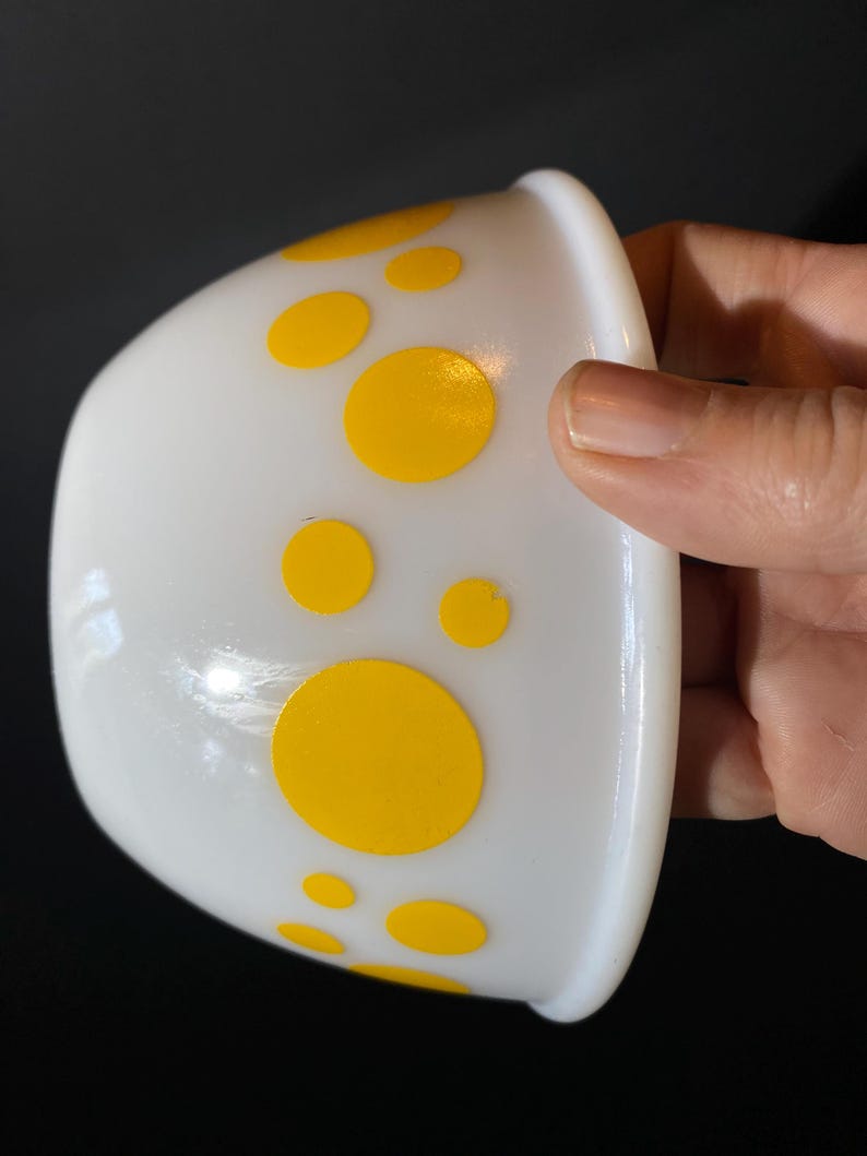 May include: White ceramic bowl with yellow polka dots. The bowl is slightly tilted and the polka dots are of varying sizes.