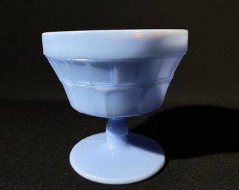 May include: A light blue glass dessert bowl with a pedestal base. The bowl has a fluted design and is made of opaque glass.