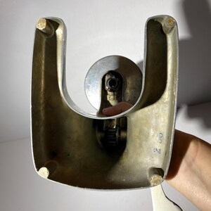 May include: A vintage silver-coloured bottle opener with a white handle. The opener has a U-shaped base and a lever that is used to open bottles. The opener has a number "24" printed on the side.