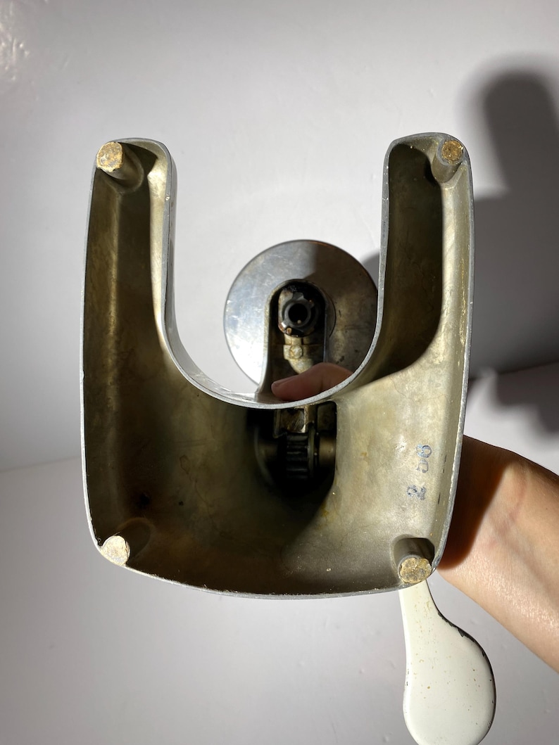 May include: A vintage silver-coloured bottle opener with a white handle. The opener has a U-shaped base and a lever that is used to open bottles. The opener has a number "24" printed on the side.