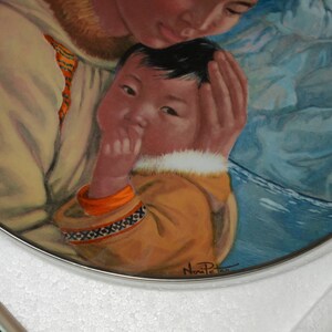 May include: A decorative plate with a painting of a mother and child. The child wears a yellow parka with orange trim and a decorative pattern. The mother wears a beige coat with fur trim. The background is blue.