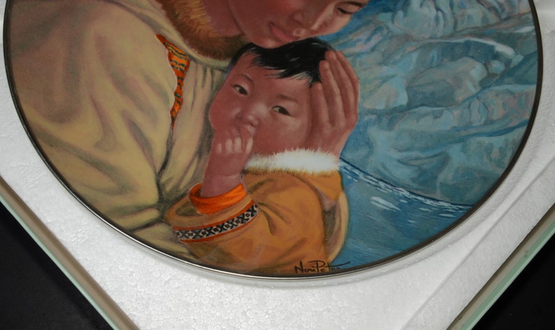 May include: A decorative plate with a painting of a mother and child. The child wears a yellow parka with orange trim and a decorative pattern. The mother wears a beige coat with fur trim. The background is blue.