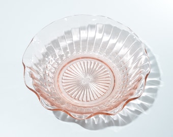 May include: A pink glass bowl with a scalloped edge and a textured bottom. The bowl has a clear glass center with a sunburst pattern.