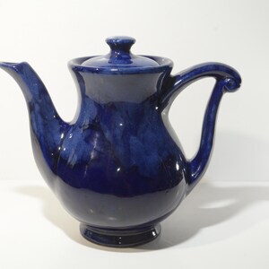 May include: A cobalt blue ceramic teapot with a rounded body and a curved handle. The teapot has a lid with a knob on top.