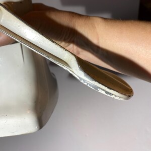 May include: White metal hand crank grinder with a handle and a base. The handle is bent at a 90-degree angle.