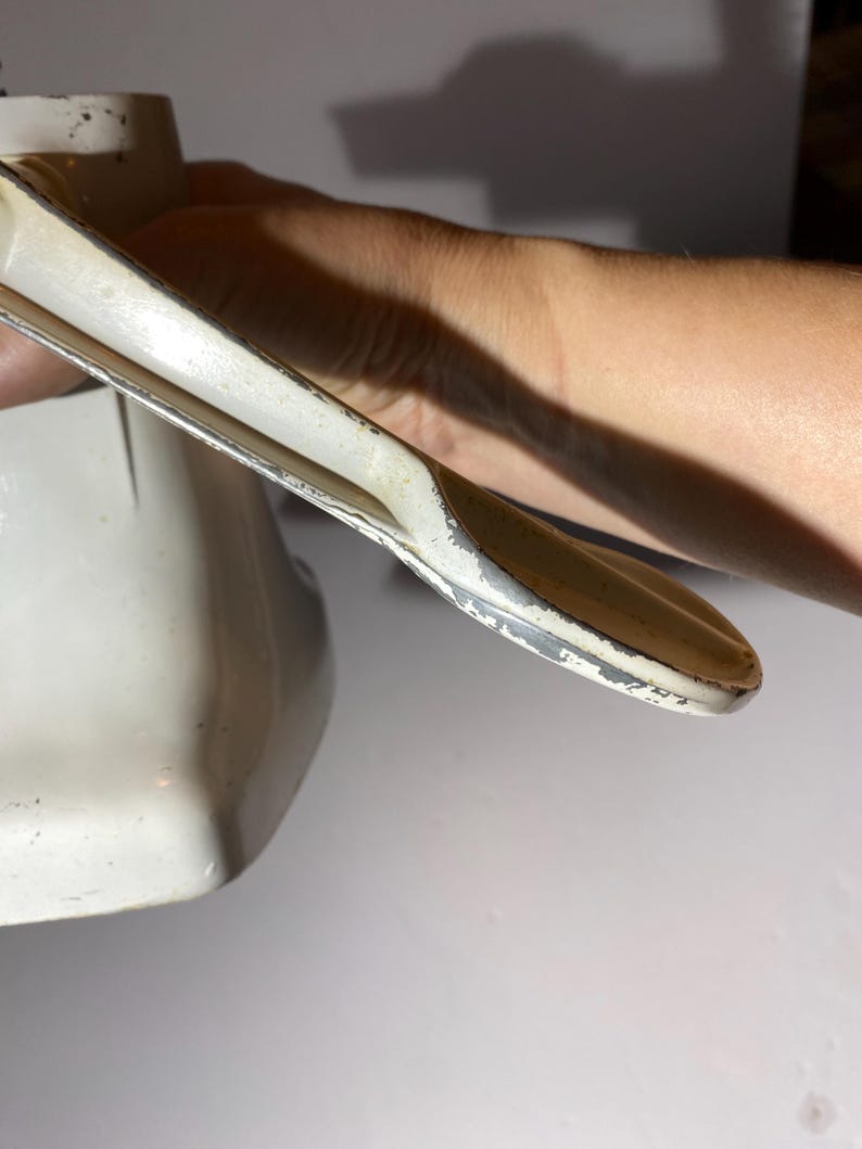 May include: White metal hand crank grinder with a handle and a base. The handle is bent at a 90-degree angle.