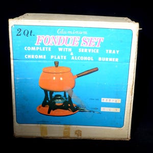 Peut inclure: Ensemble à fondue en aluminium vintage dans sa boîte d'origine. La boîte présente un fond bleu vif avec l'inscription "FONDUE SET". L'ensemble comprend une marmite à fondue orange avec une poignée en bois, un plateau de service et un brûleur à alcool chromé.