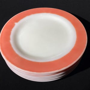 Può includere: Un set di sei piatti in vetro di latte bianco con un bordo rosa corallo.