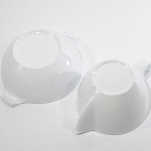 May include: Two white ceramic bowls with a unique, curved design. The bowls are empty and have a smooth, glossy finish.