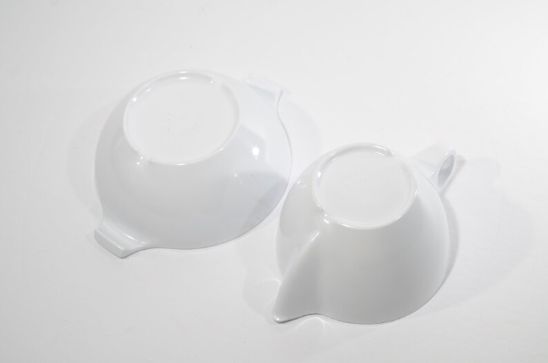 May include: Two white ceramic bowls with a unique, curved design. The bowls are empty and have a smooth, glossy finish.