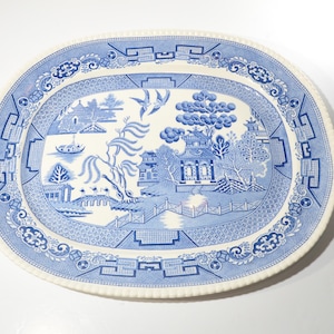 Könnte beinhalten: Eine weiße ovale Platte mit einem blauen und weißen Weidenmuster. Das Muster zeigt eine Pagode, Bäume und eine Brücke.