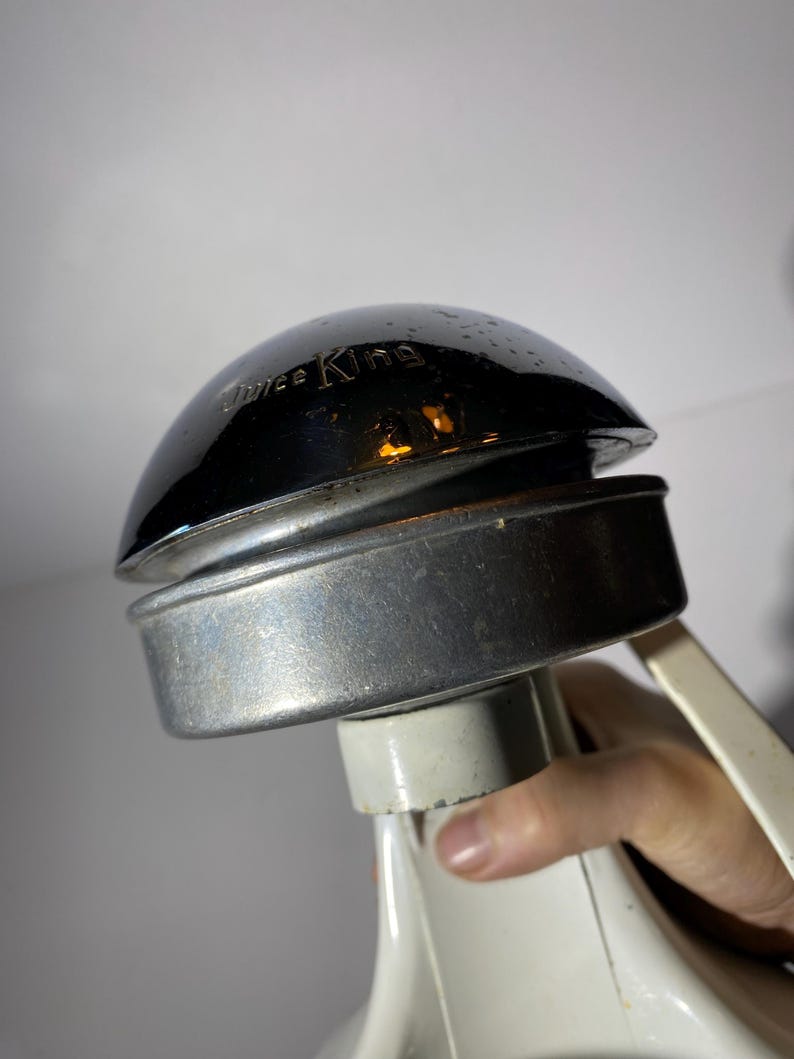 May include: Close-up of a vintage Juice King juicer with a chrome top and a white base. The juicer has a lever on the side.