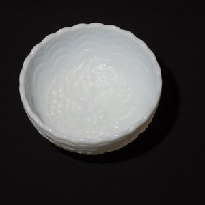 K&ouml;nnte beinhalten: Eine wei&szlig;e Sch&uuml;ssel mit gewelltem Rand und einem Traubenmuster. Die Sch&uuml;ssel besteht aus undurchsichtigem Glas und hat eine strukturierte Oberfl&auml;che. Die Sch&uuml;ssel ist rund und steht auf einer schwarzen Oberfl&auml;che.