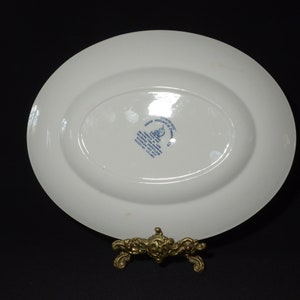 Op de afbeelding: Witte ovale serveerschaal met een blauw-wit logo aan de onderkant. Het logo bevat de tekst "Made in England" en "Royal Doulton".