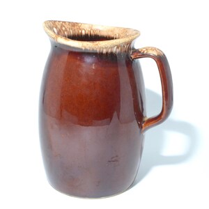 Peut inclure: Une cruche en céramique marron avec une anse. La cruche a une finition brillante et un bord de couleur plus claire. La poignée est incurvée et fixée sur le côté de la cruche. La cruche est probablement utilisée pour servir des boissons.