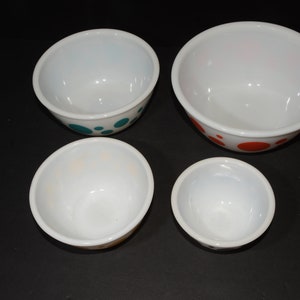 May include: Set of four white mixing bowls with colorful polka dot designs. The bowls are nested in size order, with the largest bowl having orange dots, the second largest bowl having teal dots, and the two smallest bowls having orange and yellow dots.