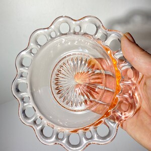 Pode incluir: Um prato de vidro rosa com uma borda festonada e um design vazado. O prato tem um centro transparente com um padr&atilde;o de estrela.