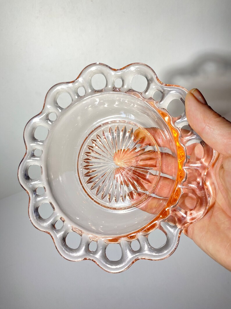 Pode incluir: Um prato de vidro rosa com uma borda festonada e um design vazado. O prato tem um centro transparente com um padr&atilde;o de estrela.