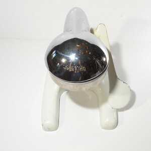 May include: White ceramic citrus juicer with a chrome top. The top has the words "Juice King" embossed on it.