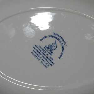 Op de afbeelding: Een wit ovaal bord met een blauw-wit logo met de tekst "COUNTRYSIDE" "ENOCH WEDGWOOD (TUNSTALL) LTD" "ENGLAND" "FOUNDED IN 1835" "TRADE MARK" "GENUINE HAND ENGRAVING" "DECORATED UNDERGLAZE" "DETERGENT AND ACID RESISTING COLORS". Het logo bevat ook een eenhoorn.