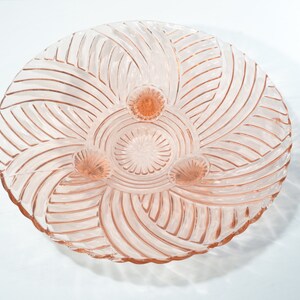 May include: A pink glass pedestal bowl with a swirl pattern and three feet.