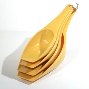 Peut inclure: Un ensemble de quatre cuillères à mesurer jaunes, emboîtées et reliées par une petite chaîne. Les cuillères sont en plastique lisse et brillant et ont une forme incurvée et allongée. L'ensemble est conçu pour mesurer les ingrédients secs.