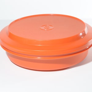 Könnte beinhalten: Orangefarbener Plastikbehälter mit Deckel. Der Behälter ist rund und hat eine glatte Oberfläche.