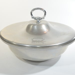 Puede incluir: Tazón de servir plateado con tapa y asa decorativa. El tazón tiene un borde con cuentas.