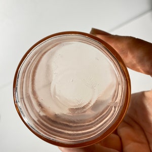 May include: The bottom of a pink glass jar with a smooth, rounded bottom and a slightly raised rim.