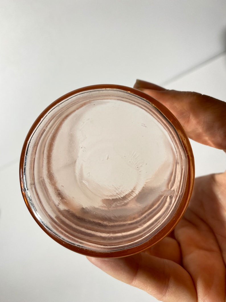May include: The bottom of a pink glass jar with a smooth, rounded bottom and a slightly raised rim.