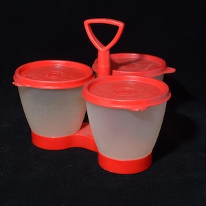 May include: A vintage red and clear plastic condiment caddy with three compartments. Each compartment has a red lid and a red base. The caddy has a handle for easy carrying. The caddy is likely from the mid-20th century.