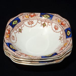 May include: A stack of four white ceramic bowls with a decorative floral and geometric pattern. The bowls have a scalloped edge and a gold rim. The pattern includes blue, brown, orange, green, and yellow details.