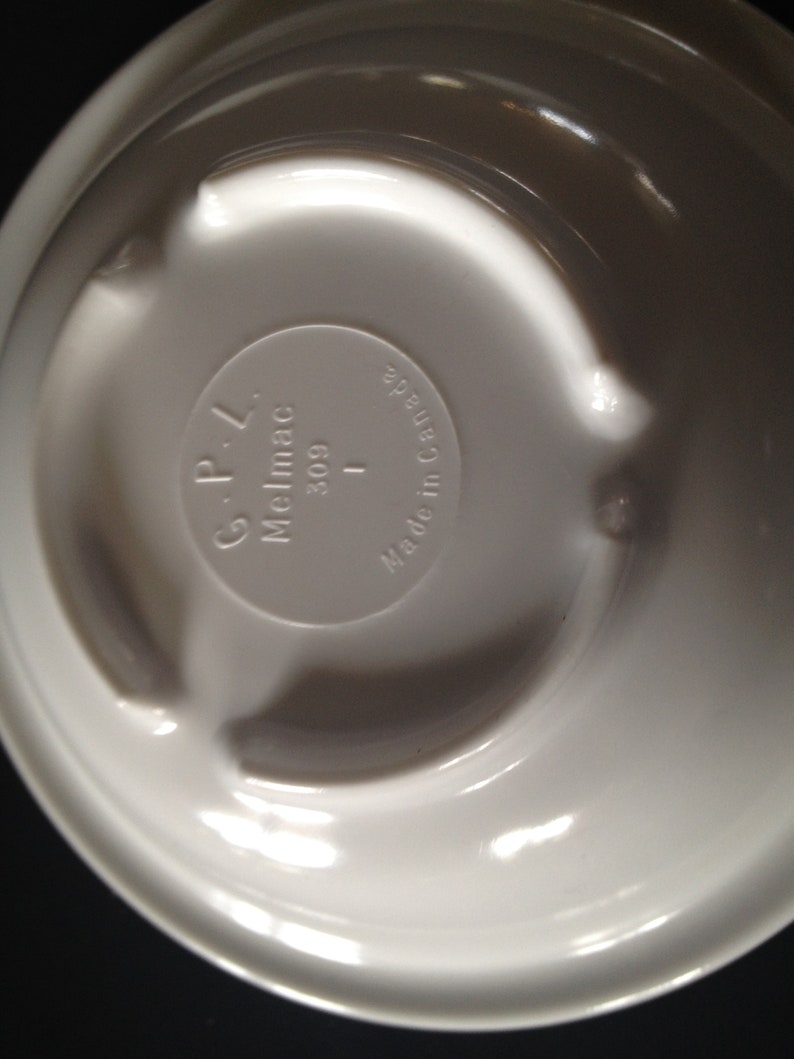 May include: White ceramic bowl with a raised rim and a circular design on the bottom. The bottom of the bowl has the text "Melmac G-P-L 309 I Made in Canada" printed on it.