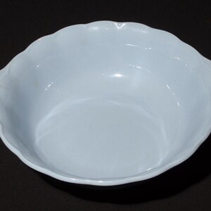 May include: A light blue, scalloped-edge bowl. The bowl has a smooth, glossy finish and a shallow depth. The rim of the bowl has a decorative, wavy design. The bowl is empty and sits on a dark surface.