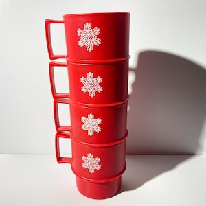 Könnte beinhalten: Ein Stapel von vier roten Plastikbechern mit weißen Schneeflocken-Designs. Die Becher sind übereinander gestapelt, wobei die Henkel der Becher in die gleiche Richtung zeigen.