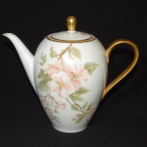 May include: White porcelain teapot with a gold handle and trim. The teapot is decorated with a floral pattern of pink and white flowers.