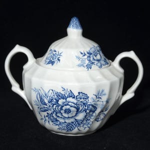 Peut inclure: Sucrier en porcelaine blanche avec couvercle, orné d'un motif floral bleu. Le sucrier a deux anses et un design facetté. Le couvercle est surmonté d'un bouton bleu. Un objet classique pour servir le sucre.